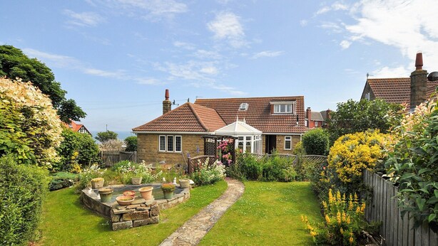 A stone house with a tiled roof, a garden with a stone pathway, and a wooden fence. - 4 bedroom accommodation in Whitby (Whitby)