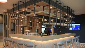 Un área de bar moderna con una isla central, taburetes y una pantalla de televisión en la pared.