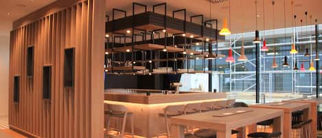 A modern bar area with a wooden partition, bar stools, and hanging pendant lights.