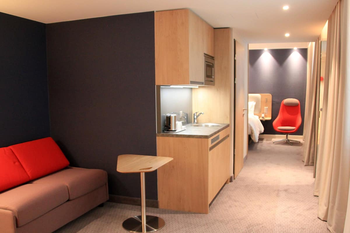 Una habitación de hotel moderna con kitchenette, una silla roja, una mesita y un sofá.