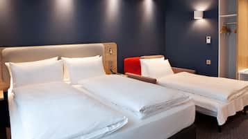 A hotel room with two beds, a wooden headboard, a red accent pillow, a white bedside table, and a built-in wardrobe with hanging space.