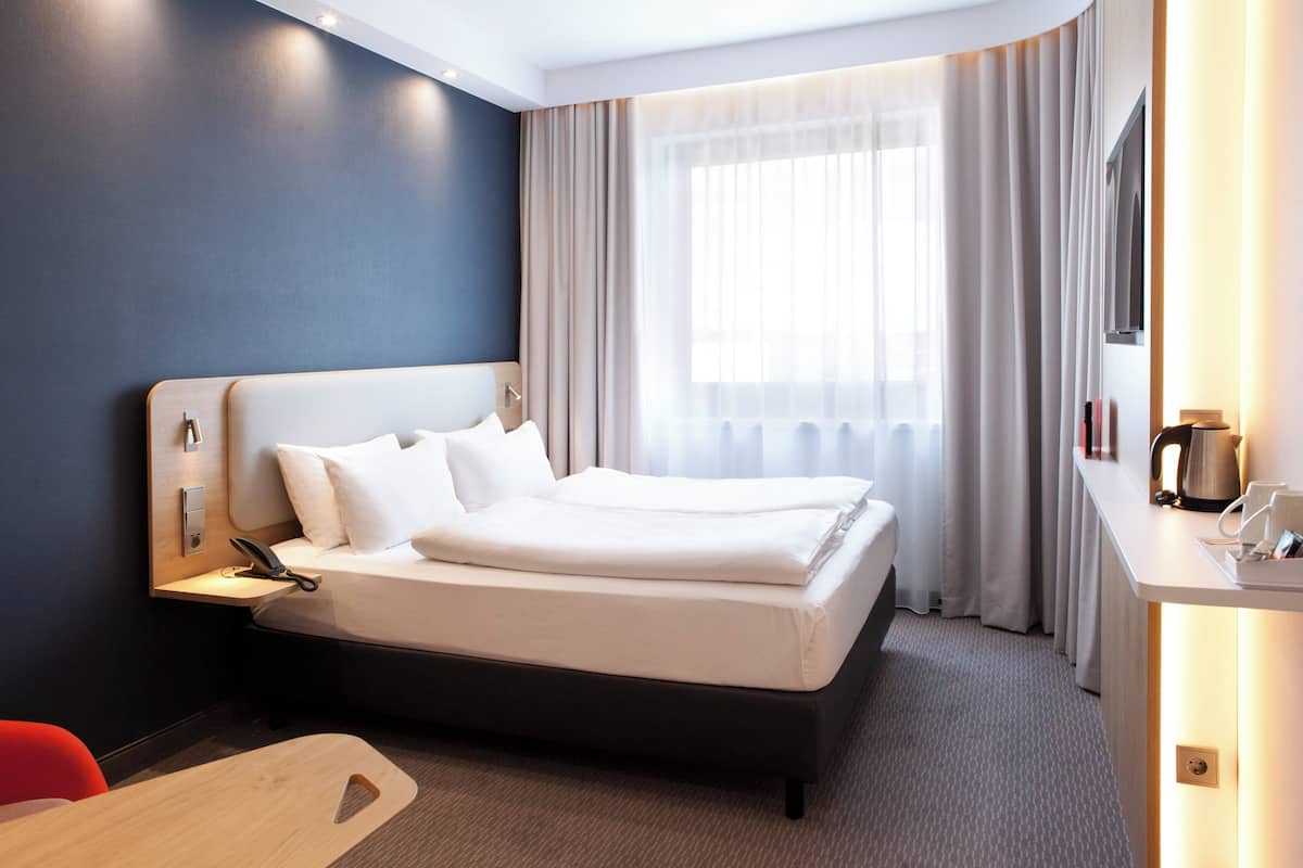Una habitación de hotel moderna con una cama grande, una mesita de noche y un escritorio con lámpara.
