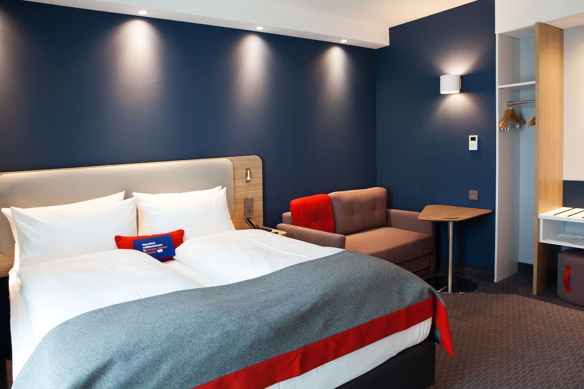 Una habitación de hotel moderna con una cama grande, un escritorio pequeño y una zona de estar.