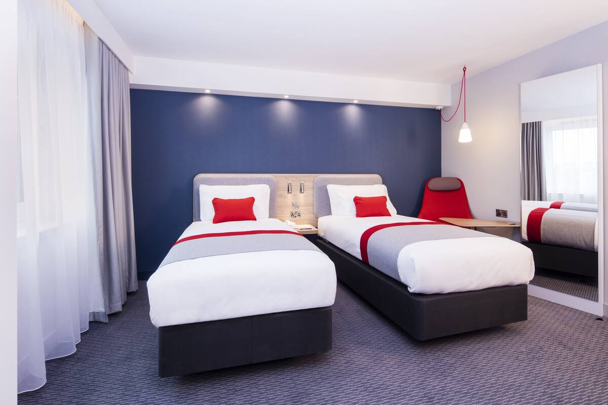 Habitación de hotel con dos camas, un escritorio, una silla y un espejo grande.
