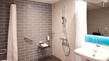 A modern bathroom with grey tiled walls, a white sink, and a shower area with a curtain.