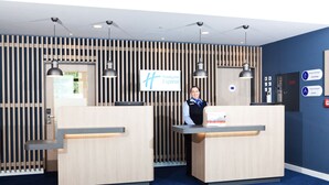 Zona de recepción de Holiday Inn Express con dos mostradores, una pared azul con listones de madera verticales y un cartel que indica la oficina del gerente general.
