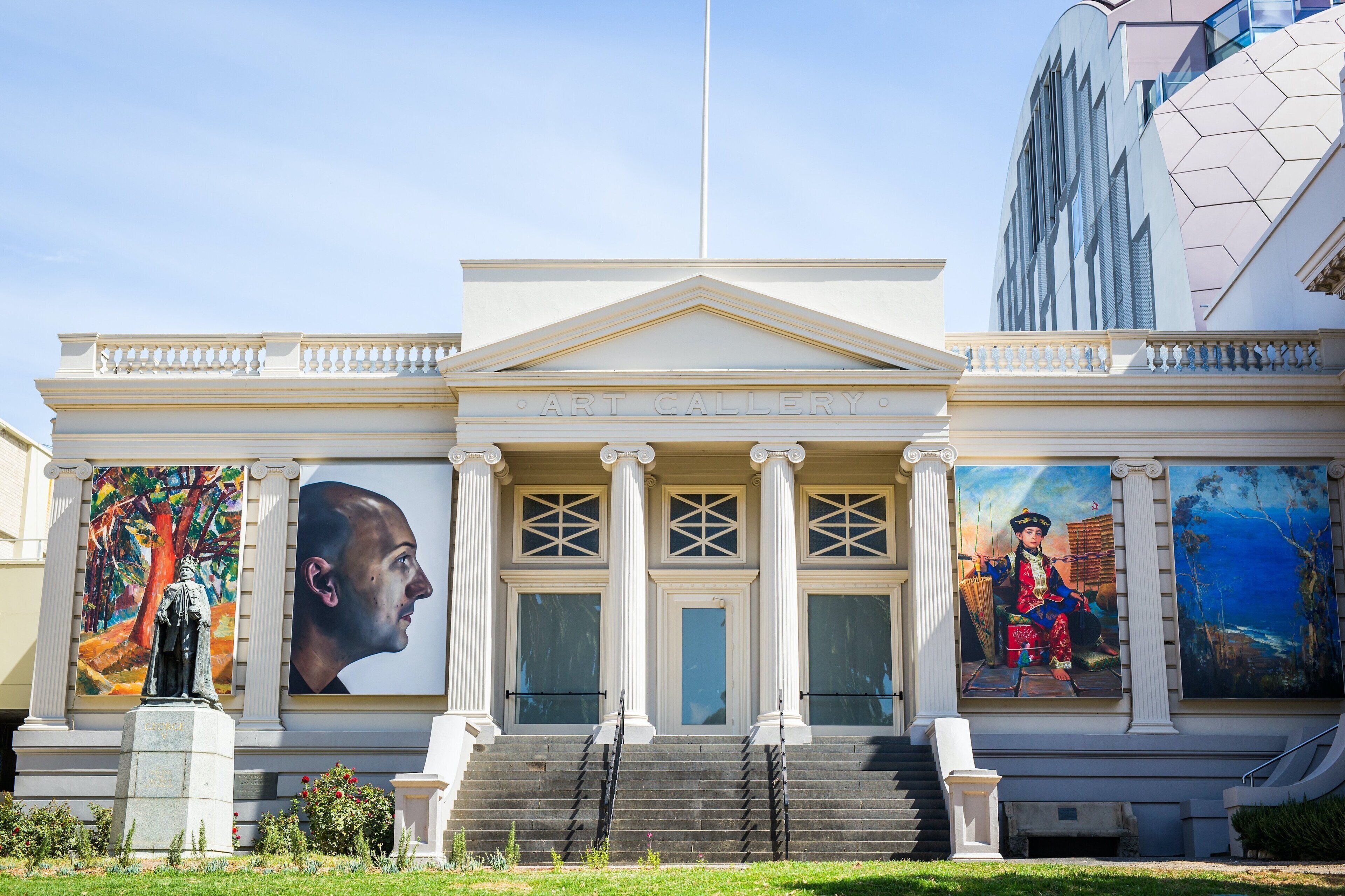 A building with a classical architectural style, featuring a central entrance with steps, flanked by columns, and large murals on the walls.