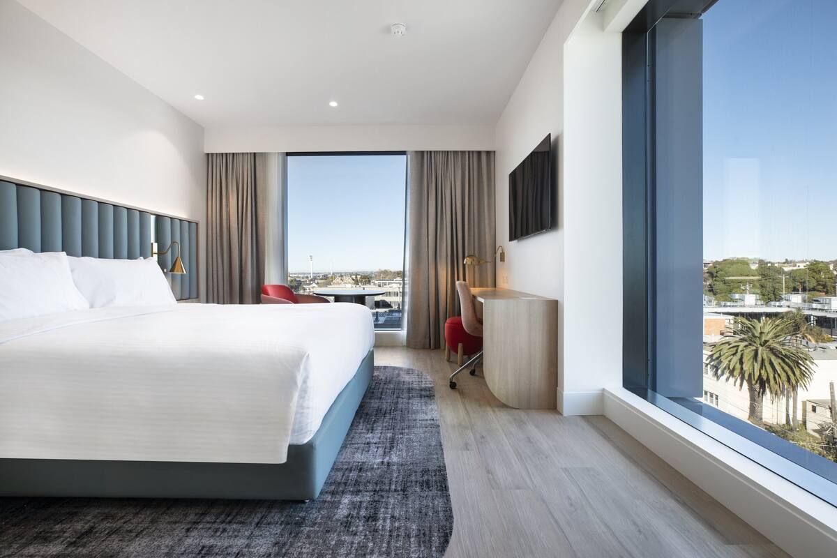 A modern hotel room with a large bed, a desk, and a view of the city.