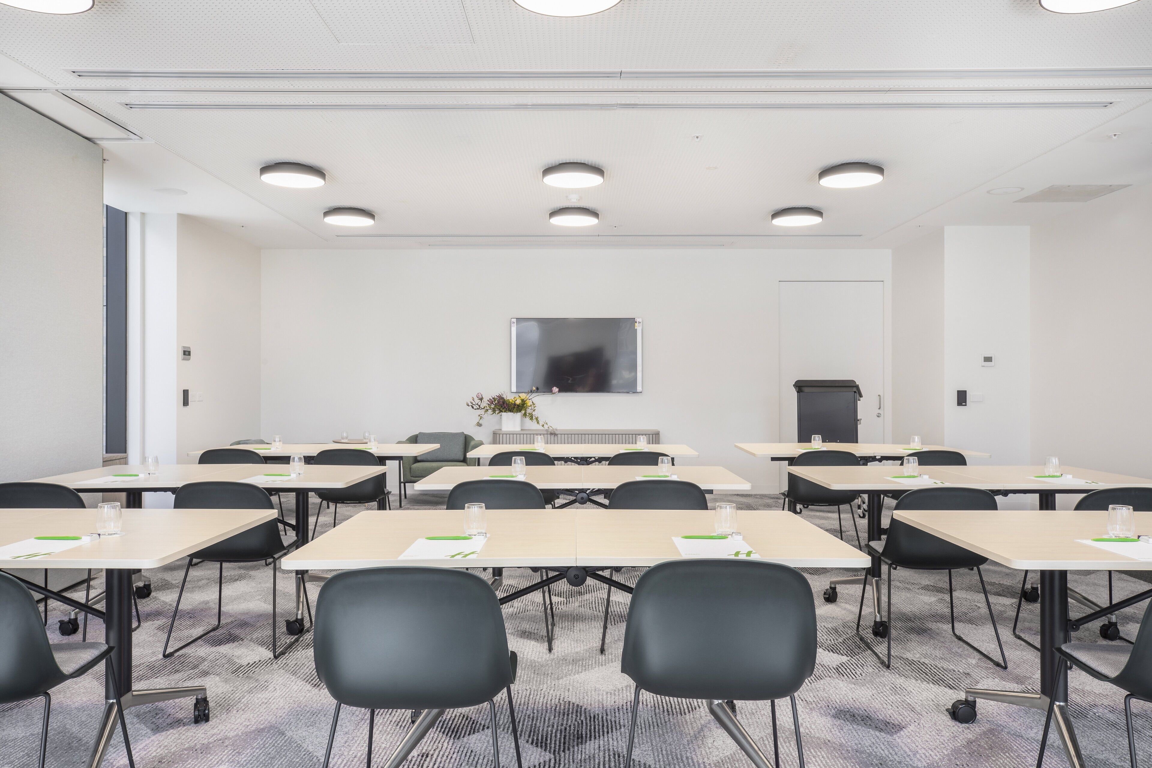 A conference room with multiple tables and chairs, a large screen, and a door.