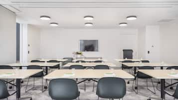 Une salle de conférence équipée de plusieurs tables et chaises, d’un grand écran et d’une porte.