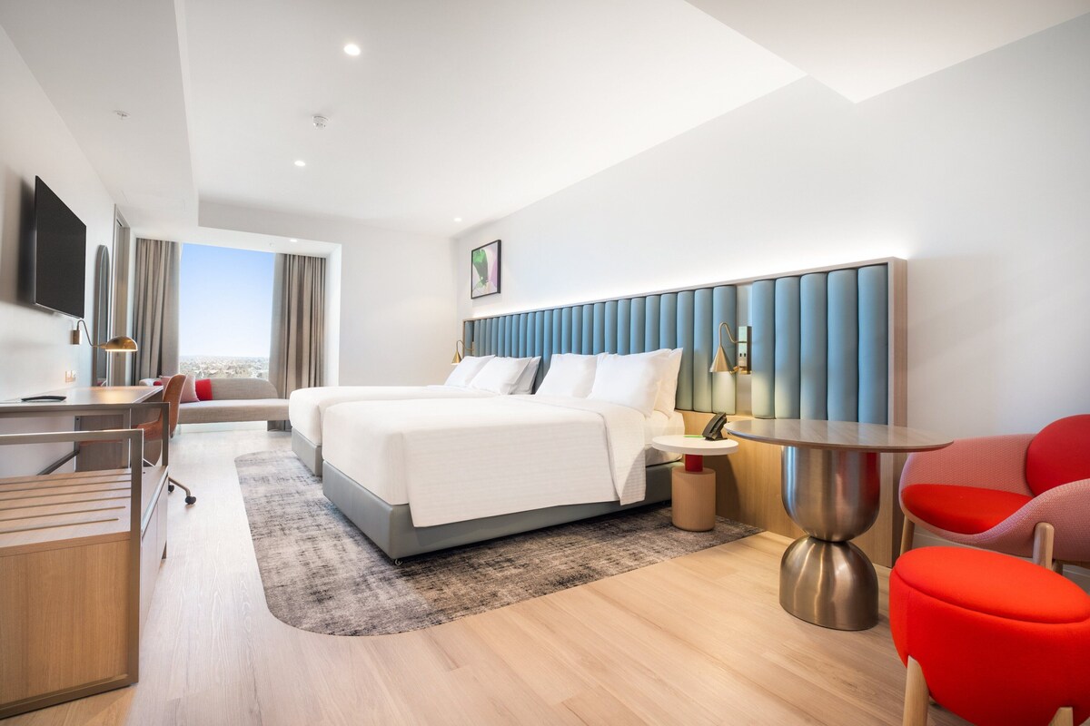 A modern hotel room with a large bed, a desk, a chair, and a dining table.