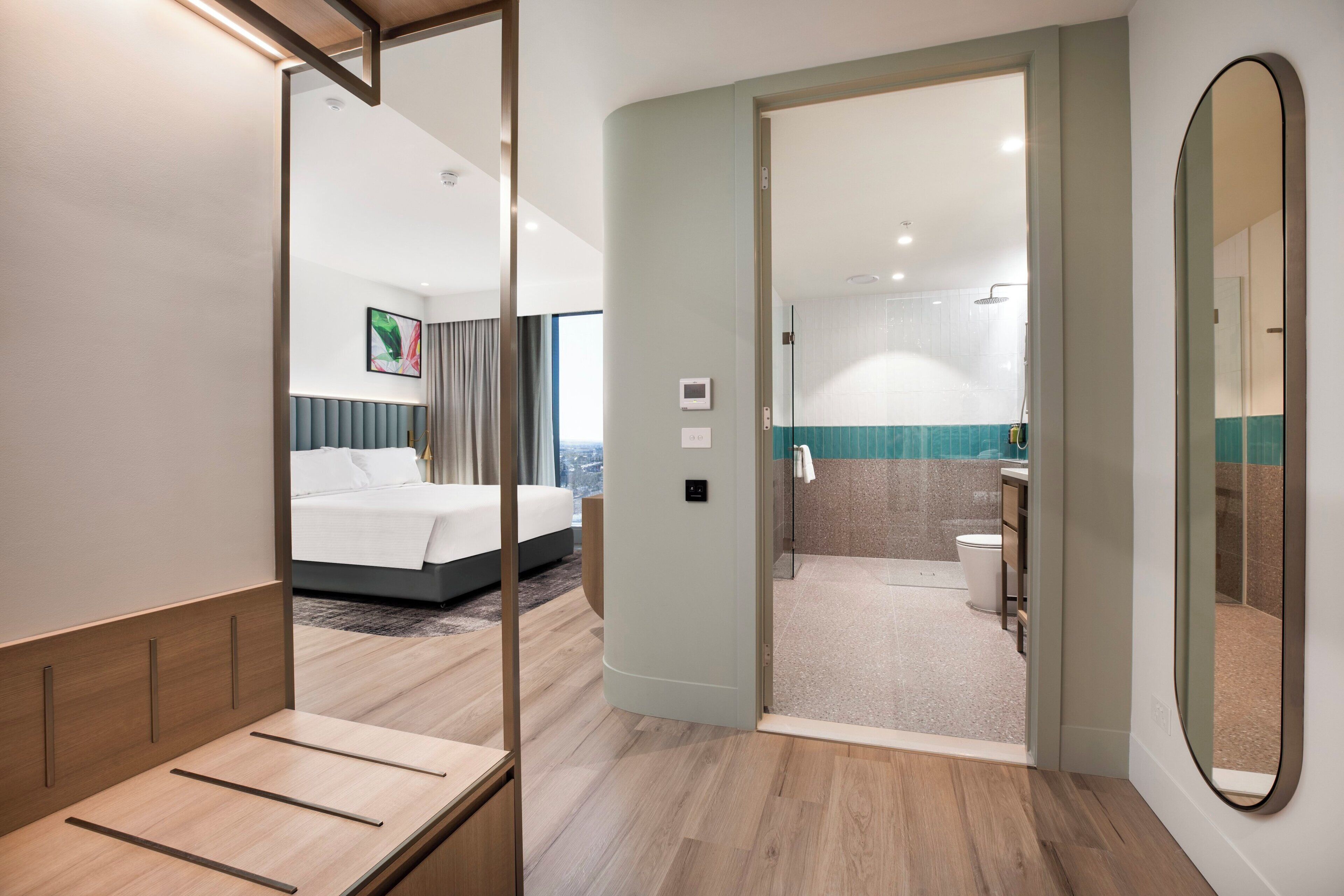 A modern hotel room with a bed, a bathroom with a shower, and a view of the city.