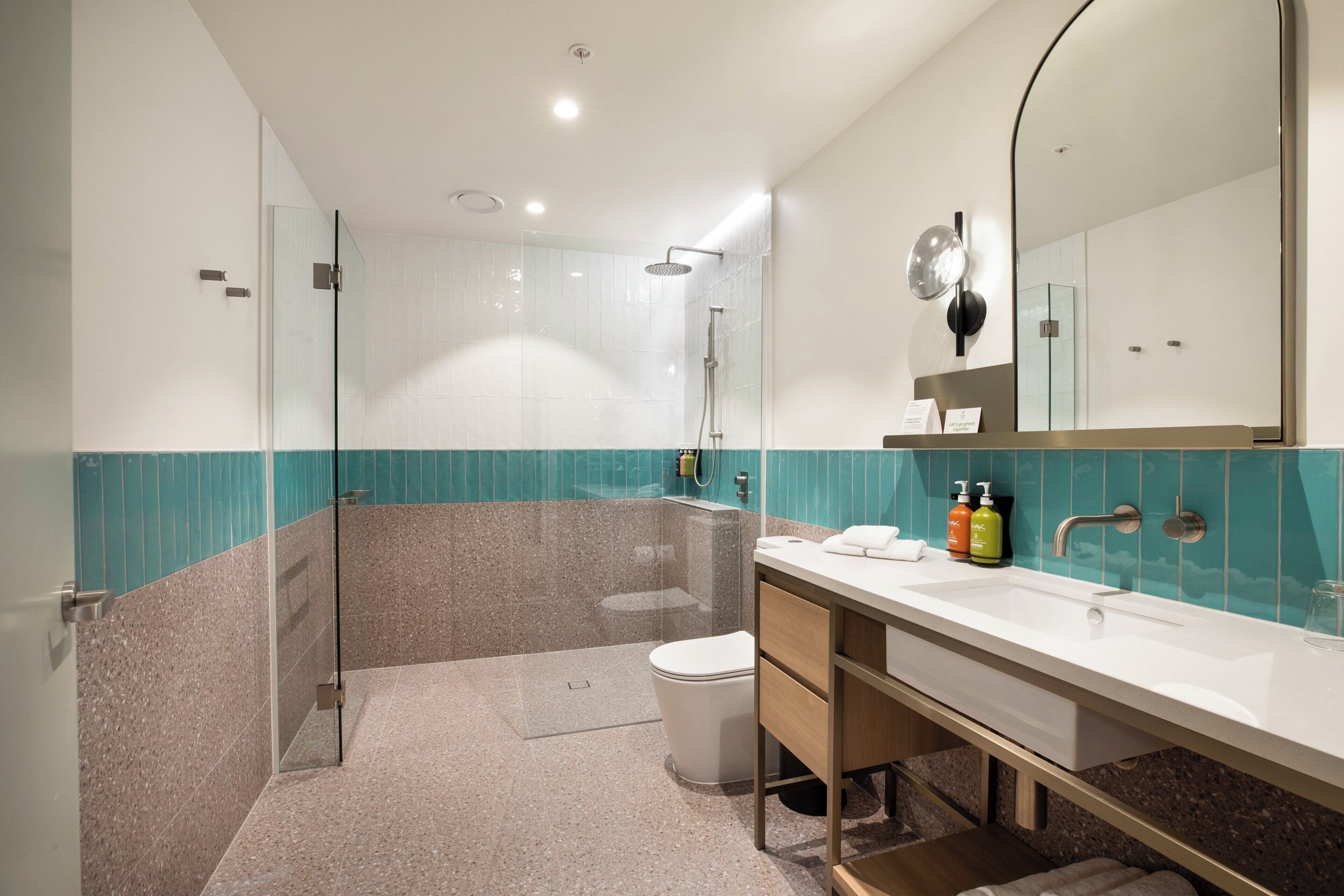 Ein modernes Badezimmer mit einer einteiligen Duschkabine, einer weißen Toilette, einem Waschbecken mit Spiegel und einem Waschtisch mit Pflegeprodukten.