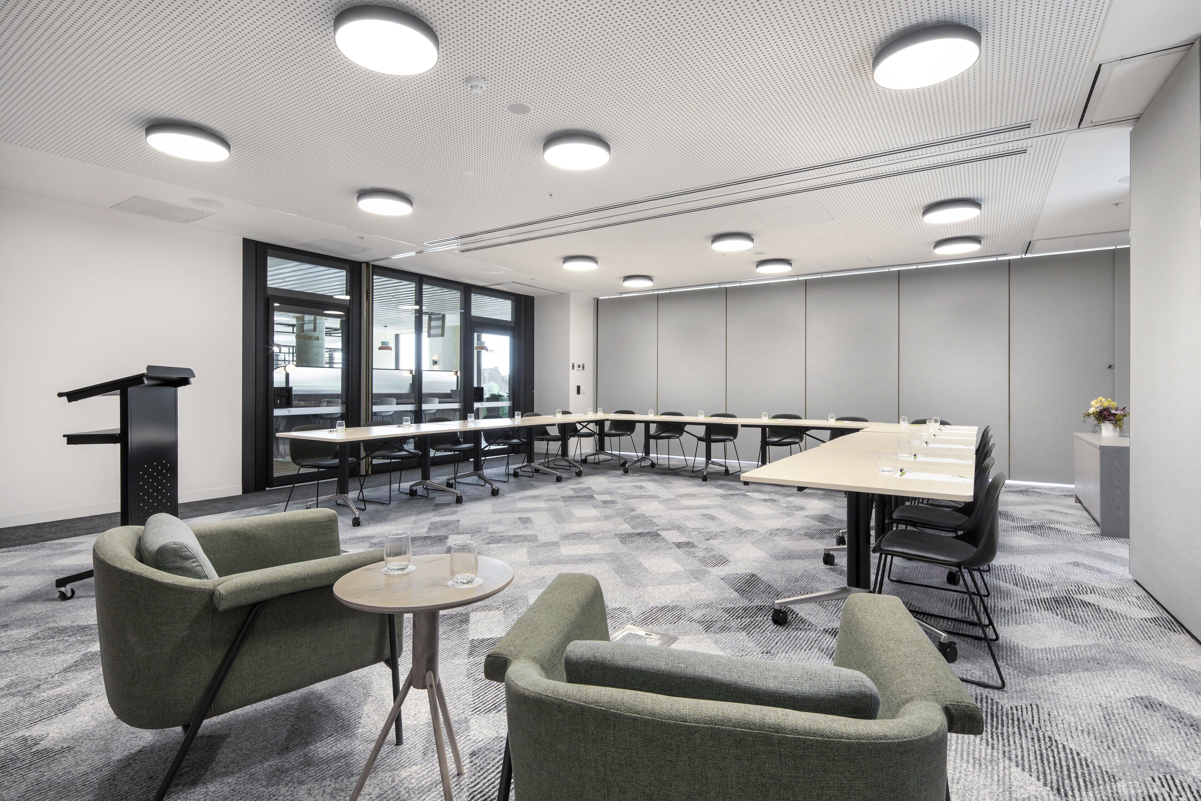 A conference room with a long table, several chairs, a podium, and a small table with a glass.