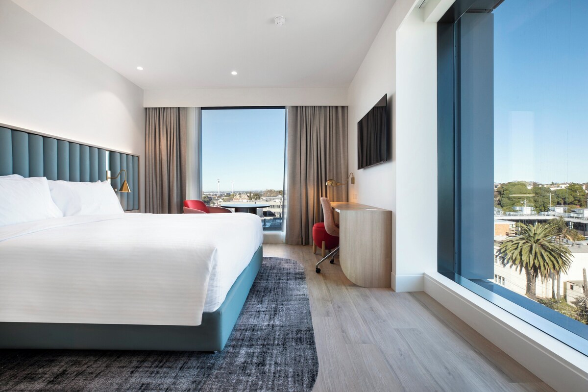 A modern hotel room with a large bed, a desk, and a view of the city.