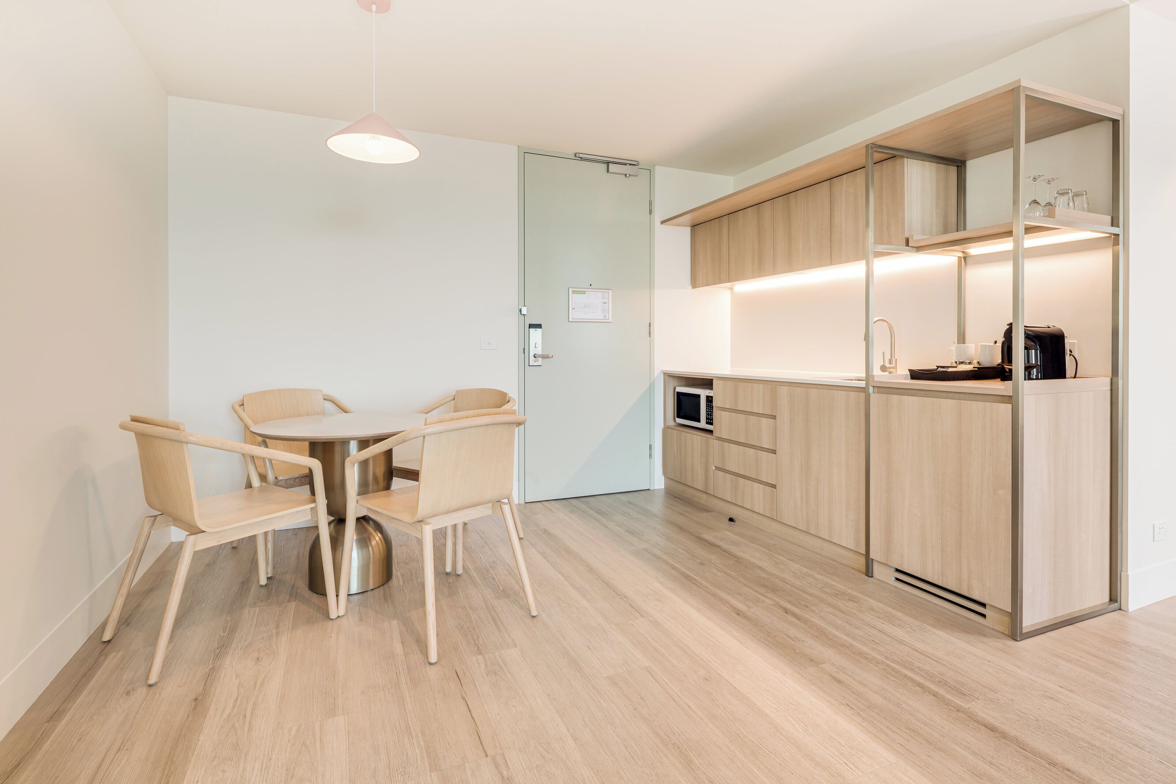A modern kitchen with wooden cabinets, a dining table with chairs, and a microwave.