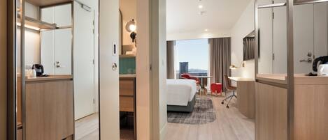 A hotel room with a bed, desk, chair, and a view of the cityscape.