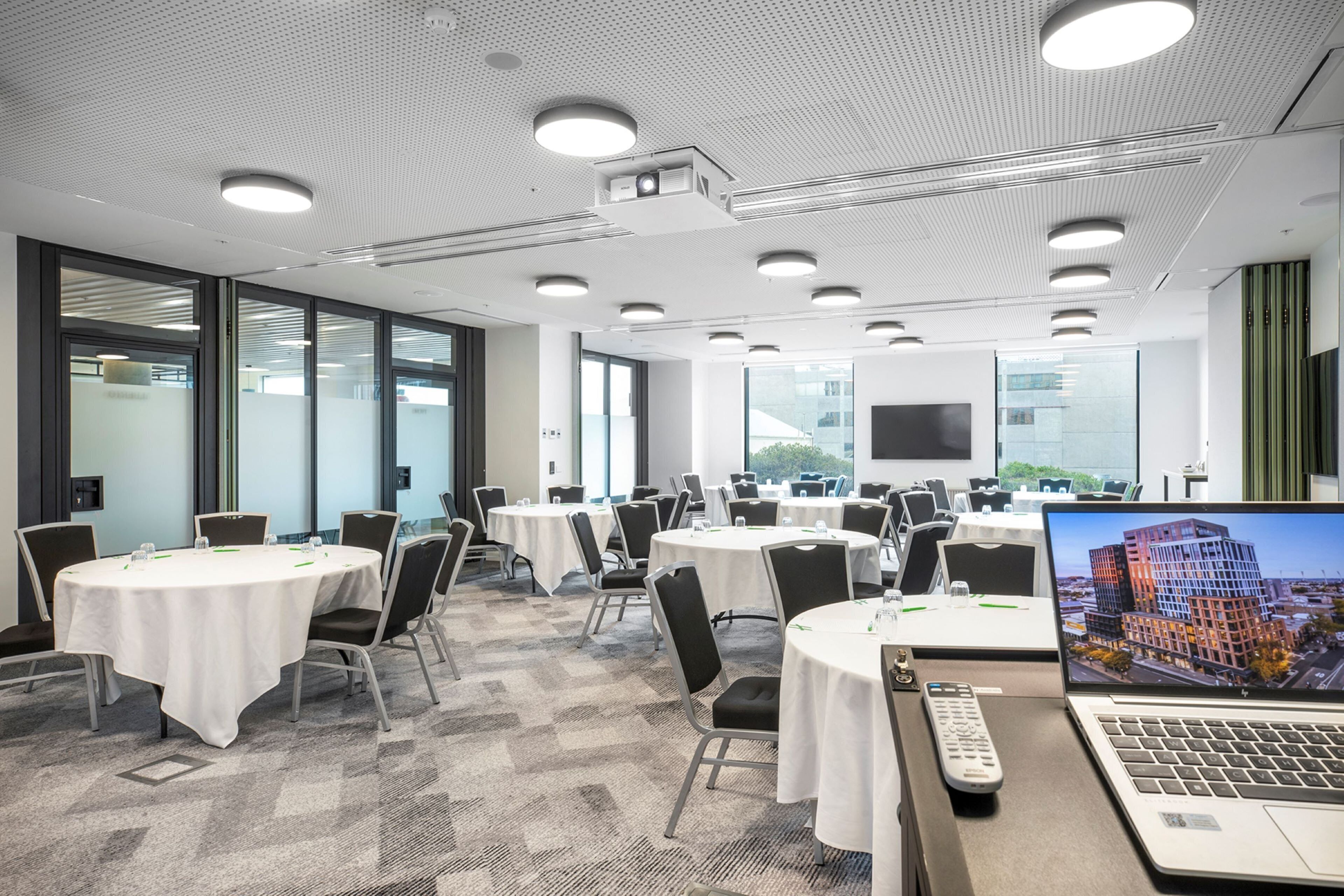 A conference room with multiple tables, chairs, and a laptop displaying a cityscape.