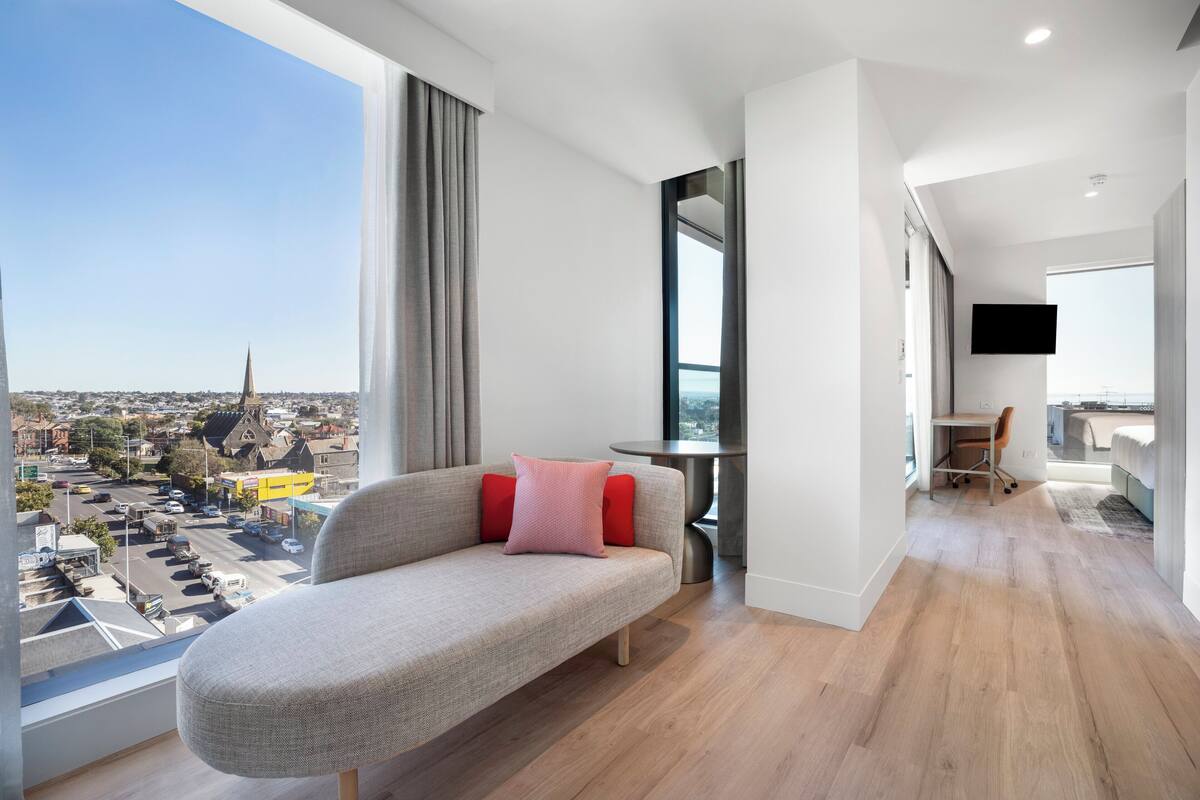 A modern living room with a sofa, a dining area, and a view of the cityscape.