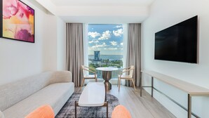 A modern hotel room with a sofa, two chairs, a small table, a TV, and a large window with a city view. - Holiday Inn & Suites Geelong by IHG (Geelong)