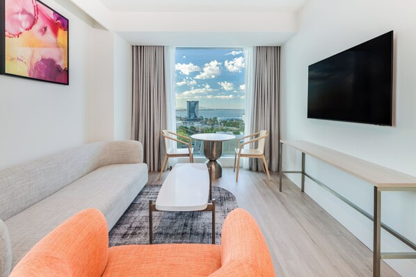 A modern hotel room with a sofa, two chairs, a small table, a TV, and a large window with a city view. - Holiday Inn & Suites Geelong by IHG (Geelong)