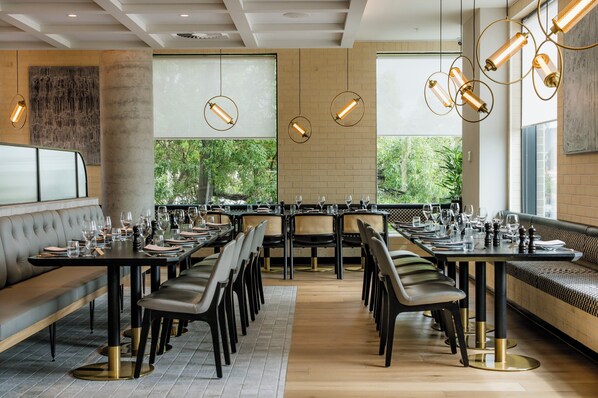Um restaurante moderno com uma mesa comunitária grande, assentos acolchoados e iluminação pendente.