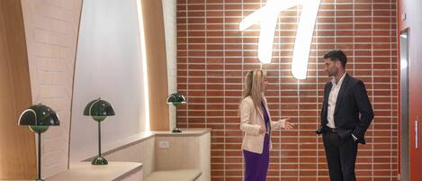 A lobby with a large illuminated 'H' sign, a curved reception desk, and two green floor lamps.