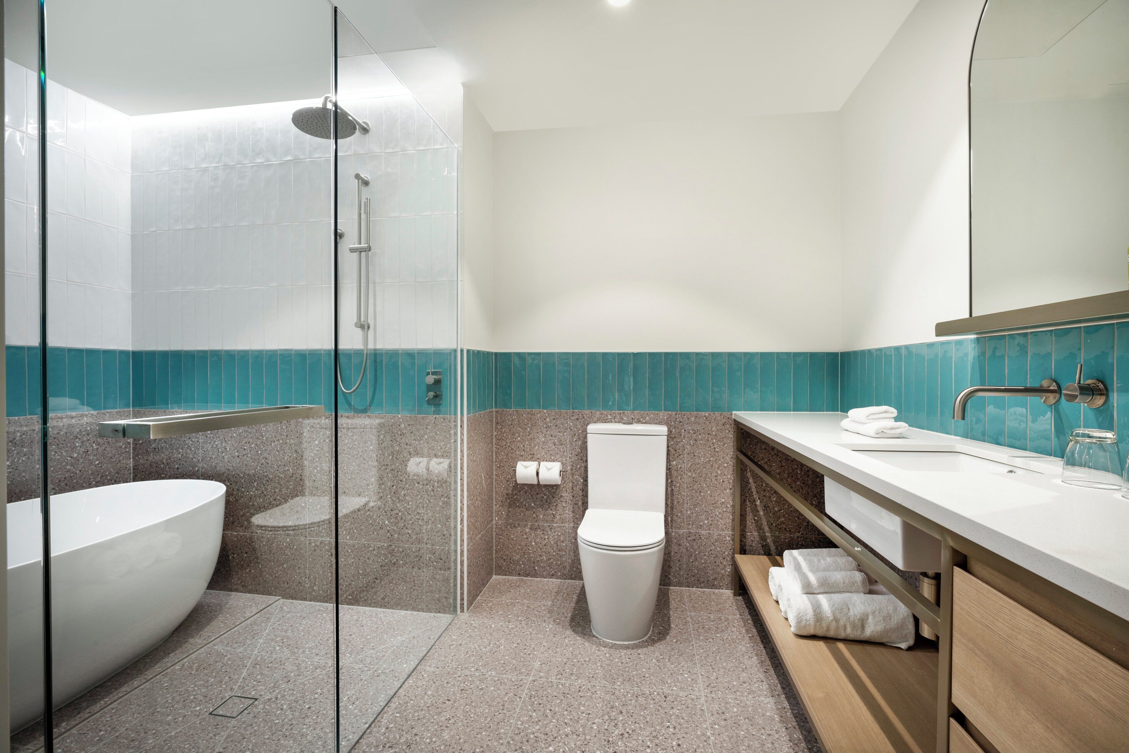Un baño moderno con ducha envuelta en vidrio, una bañera independiente y un tocador con espejo.