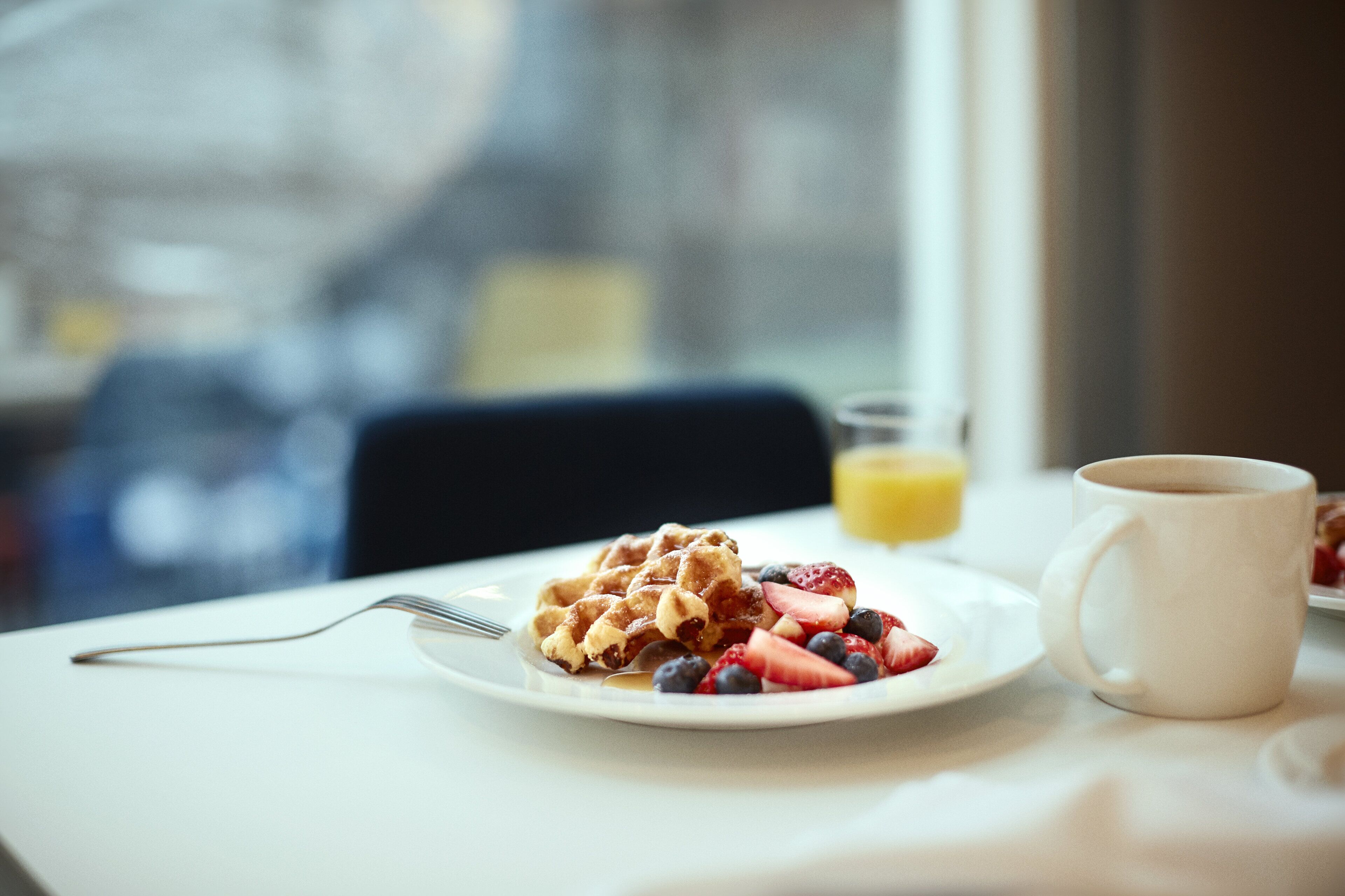 Ein Frühstückstisch mit Waffeln, Erdbeeren und Blaubeeren auf einem Teller, einer Kaffeetasse und einem Glas Orangensaft.