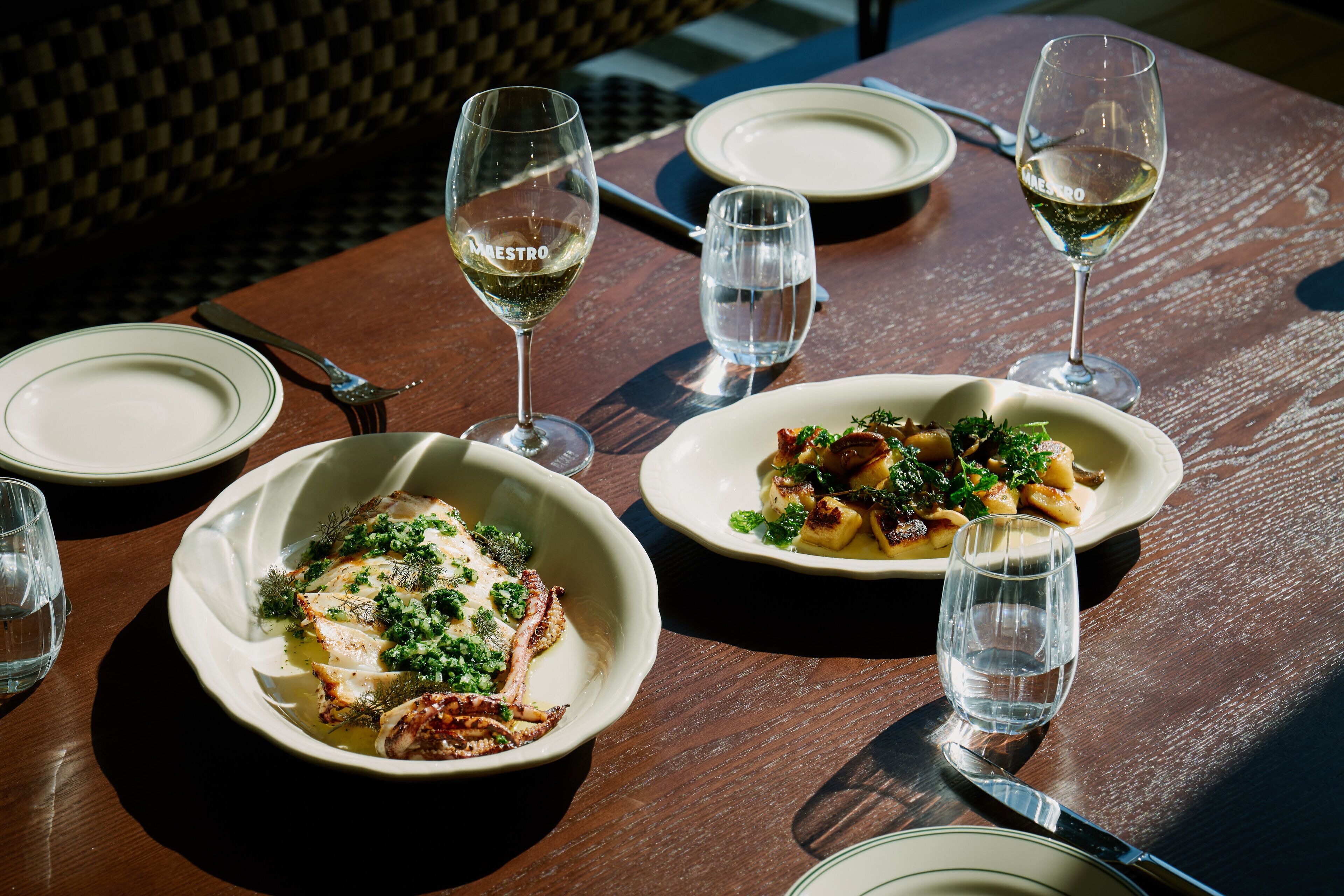 A dining table with plates of food, wine glasses, and cutlery.