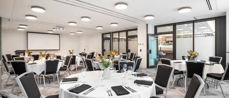 A conference room with round tables, black chairs, and white tablecloths.