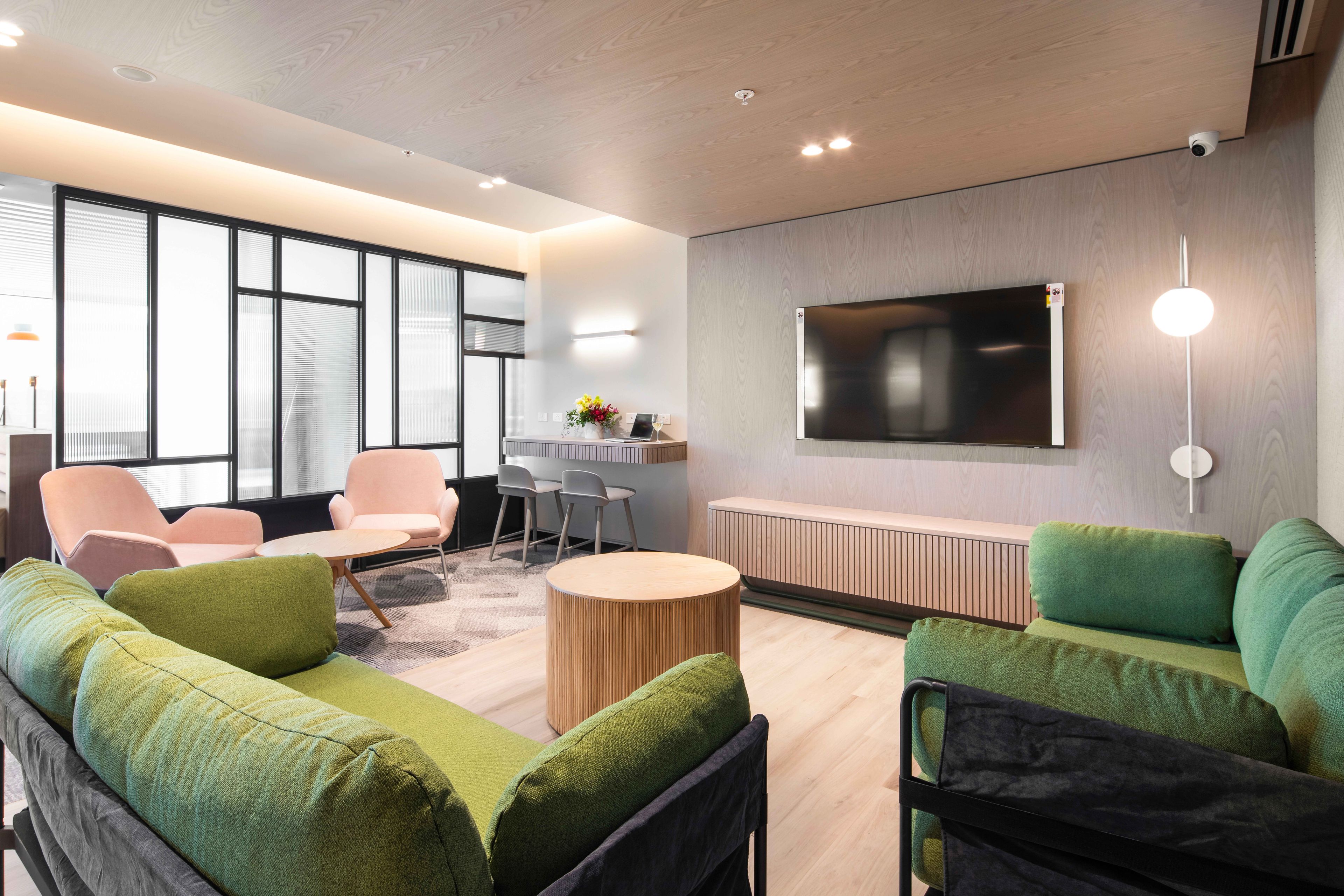 A modern lounge area with a sofa, chairs, a small table, and a TV mounted on the wall.