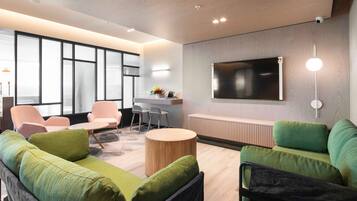 A modern lounge area with a sofa, chairs, a small table, and a TV mounted on the wall.