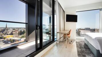 Una habitación de hotel moderna con un amplio ventanal corredero, una cama, un escritorio y un televisor.