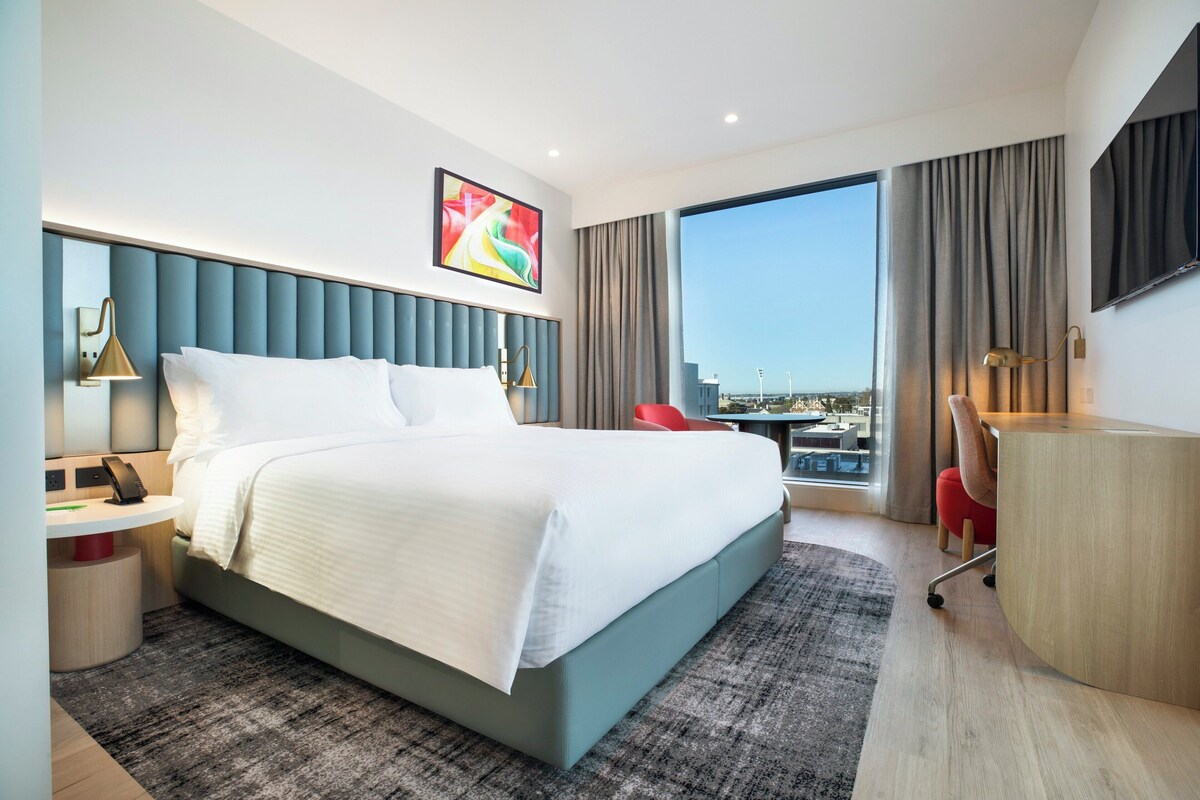 Een moderne hotelkamer met een groot bed, een bureau, een stoel, een flatscreen televisie en uitzicht over de stad.