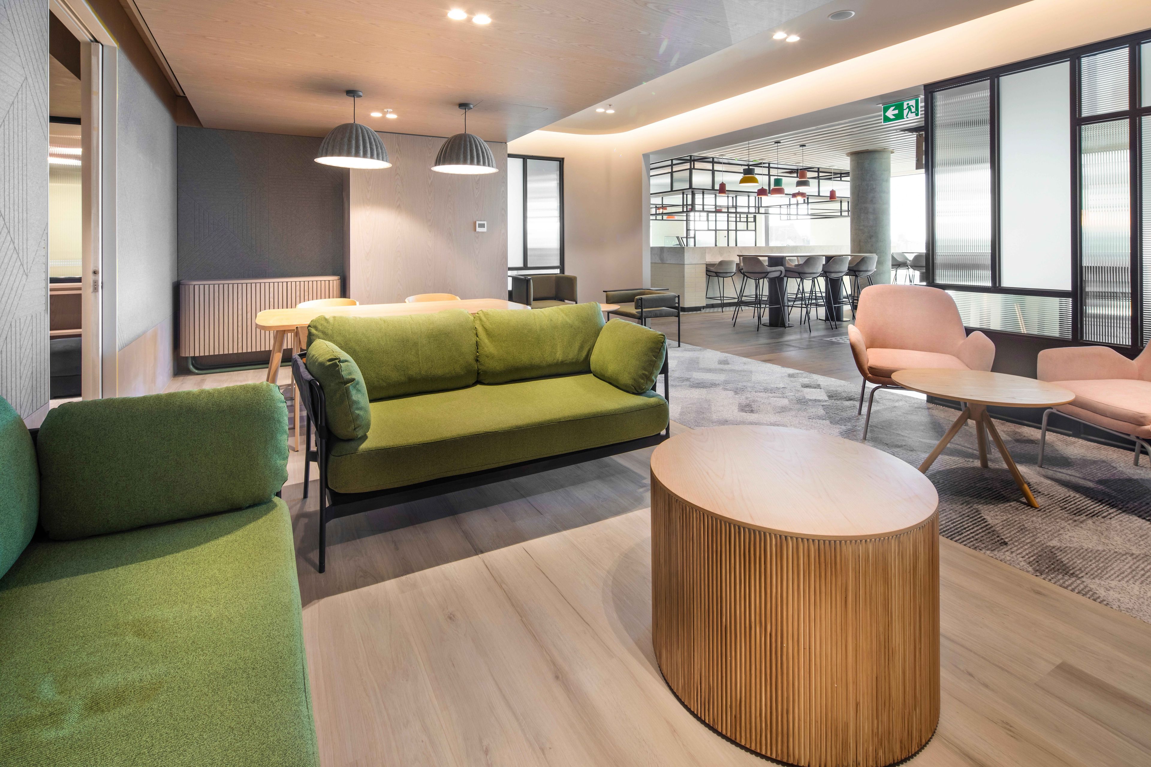 Ein moderner Lounge-Bereich mit einem grünen Sofa, einem runden Holztisch und einer Sitzecke mit Sesseln.