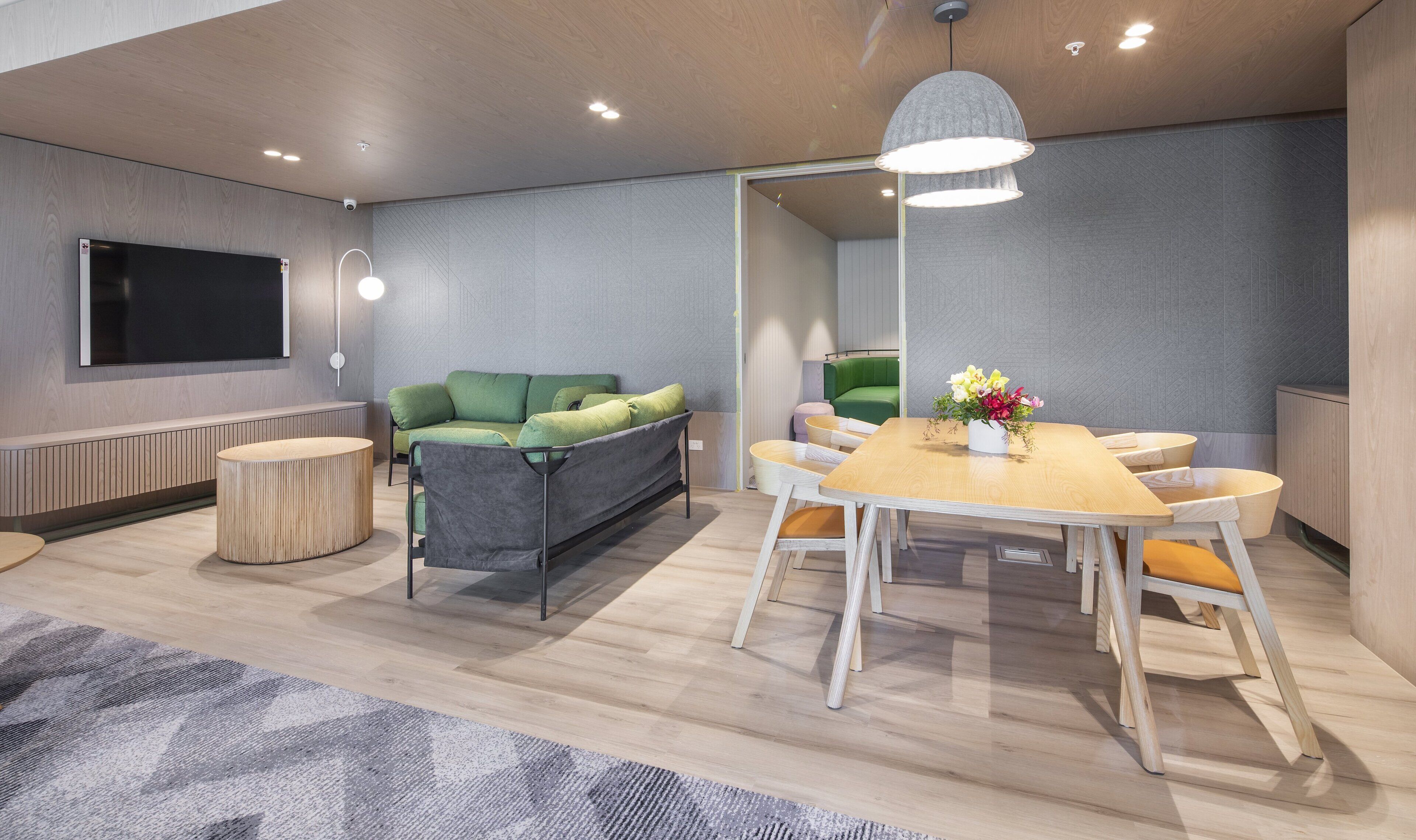 Ein moderner Konferenzraum mit großem Tisch, einem grünen Sofa und einem Fernseher an der Wand.