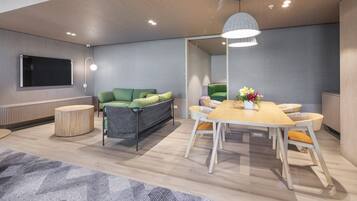 Ein moderner Konferenzraum mit großem Tisch, einem grünen Sofa und einem Fernseher an der Wand.