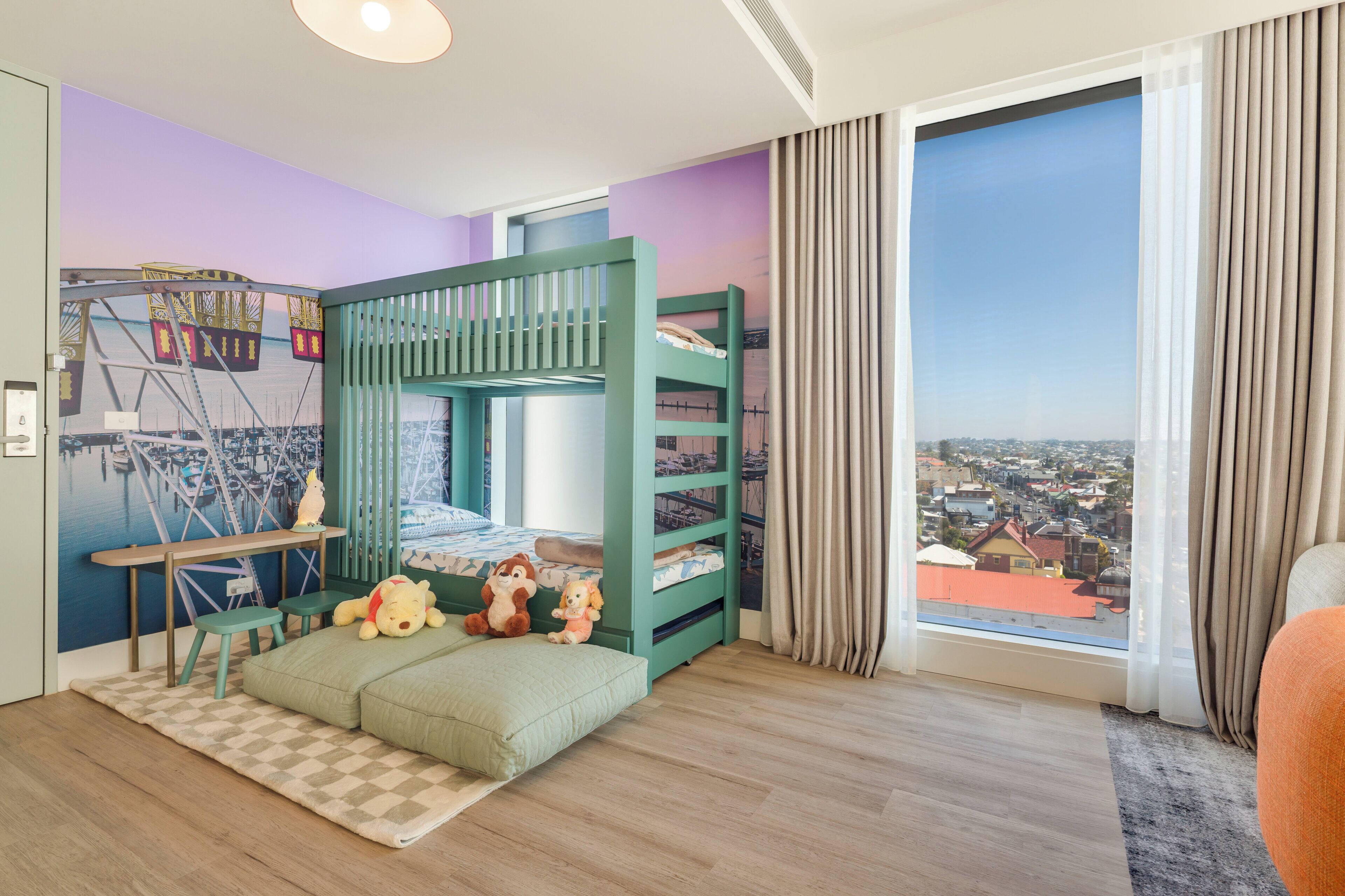 Habitación infantil con literas, juguetes, un escritorio y vistas a un paisaje urbano.