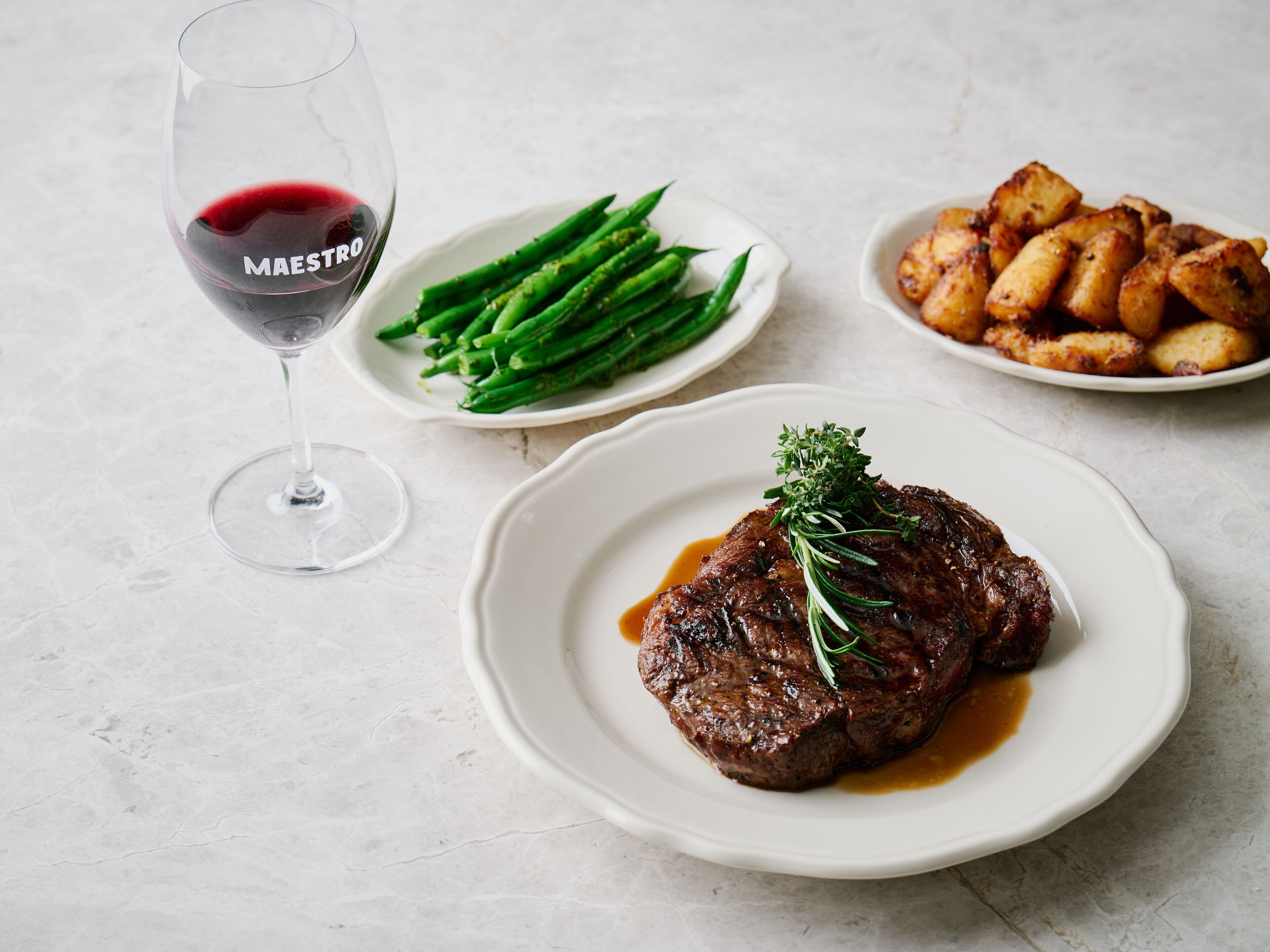 Un steak garni, des asperges et des pommes de terre rôties, le tout présenté dans une assiette, accompagné d’un verre de vin rouge.