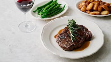 Un plato de carne con guarnición, espárragos y papas asadas, junto a una copa de vino tinto.