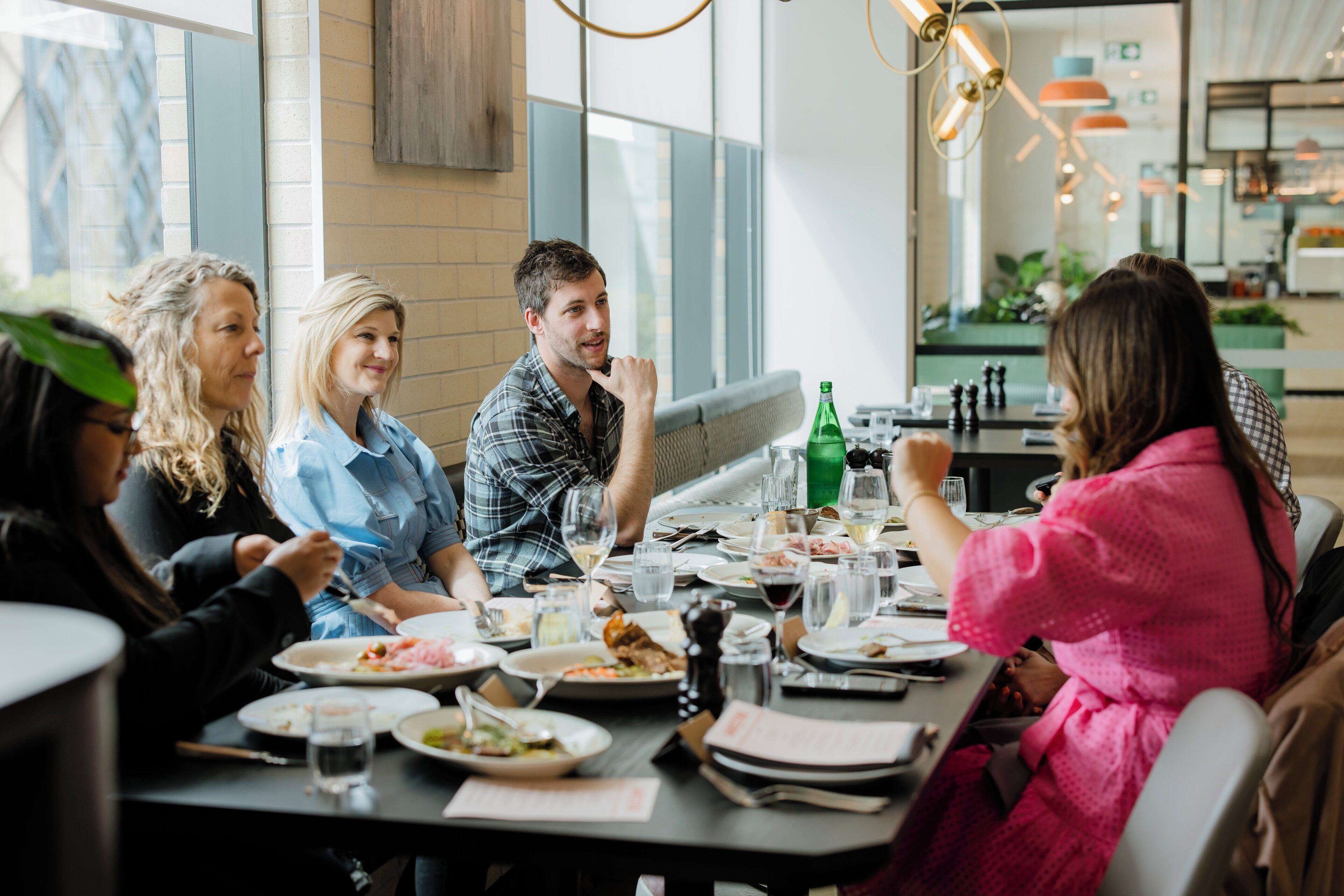 Un gruppo di persone cena in un ristorante dall'arredamento moderno, con ampie vetrate e lampade di design.