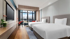 Una habitación de hotel moderna con dos camas, un escritorio con televisor y un amplio ventanal con vista a la ciudad.