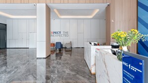 Una recepción moderna con un mostrador de mármol, una zona de estar con sillas y una pared con el texto "EXPECT THE INEXPECTED".