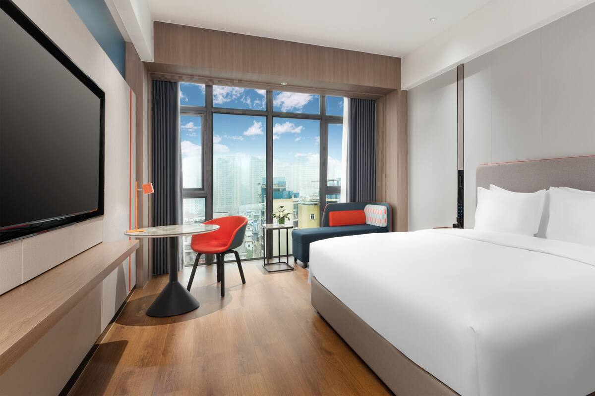 A modern hotel room with a large bed, a TV, a desk, and a chair.