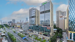 A modern hotel with a prominent sign, surrounded by high-rise buildings and a busy urban street.