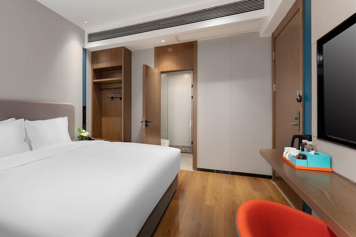 A hotel room with a large bed, a desk with a chair, and a wardrobe.