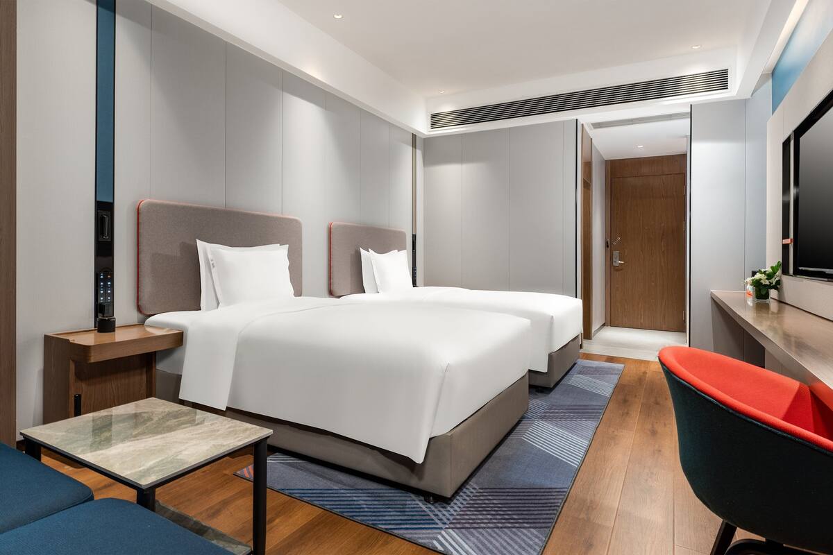 A modern hotel room with a large bed, a desk, a chair, and a TV.