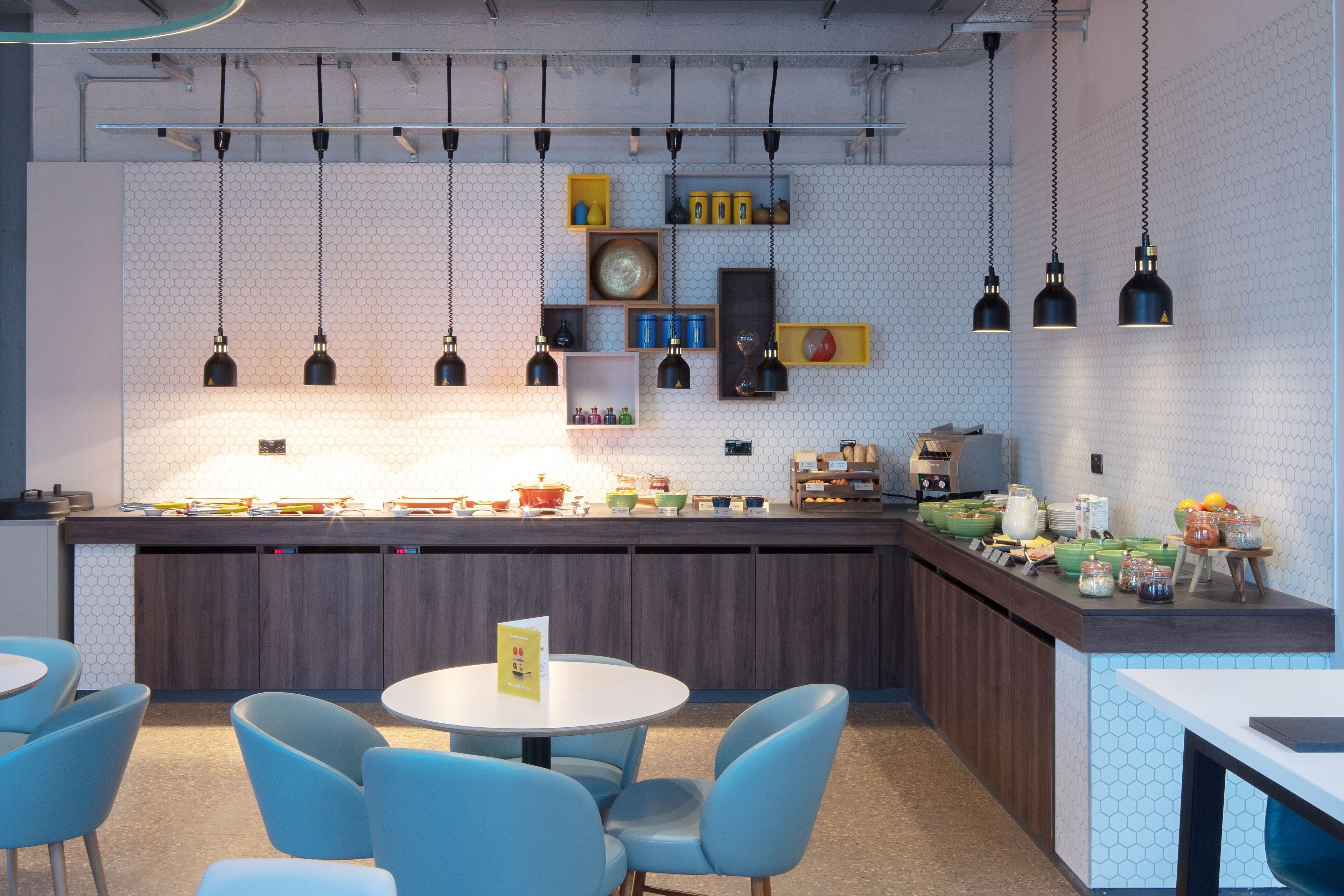 A modern kitchen with a central island, blue chairs, and hanging pendant lights.