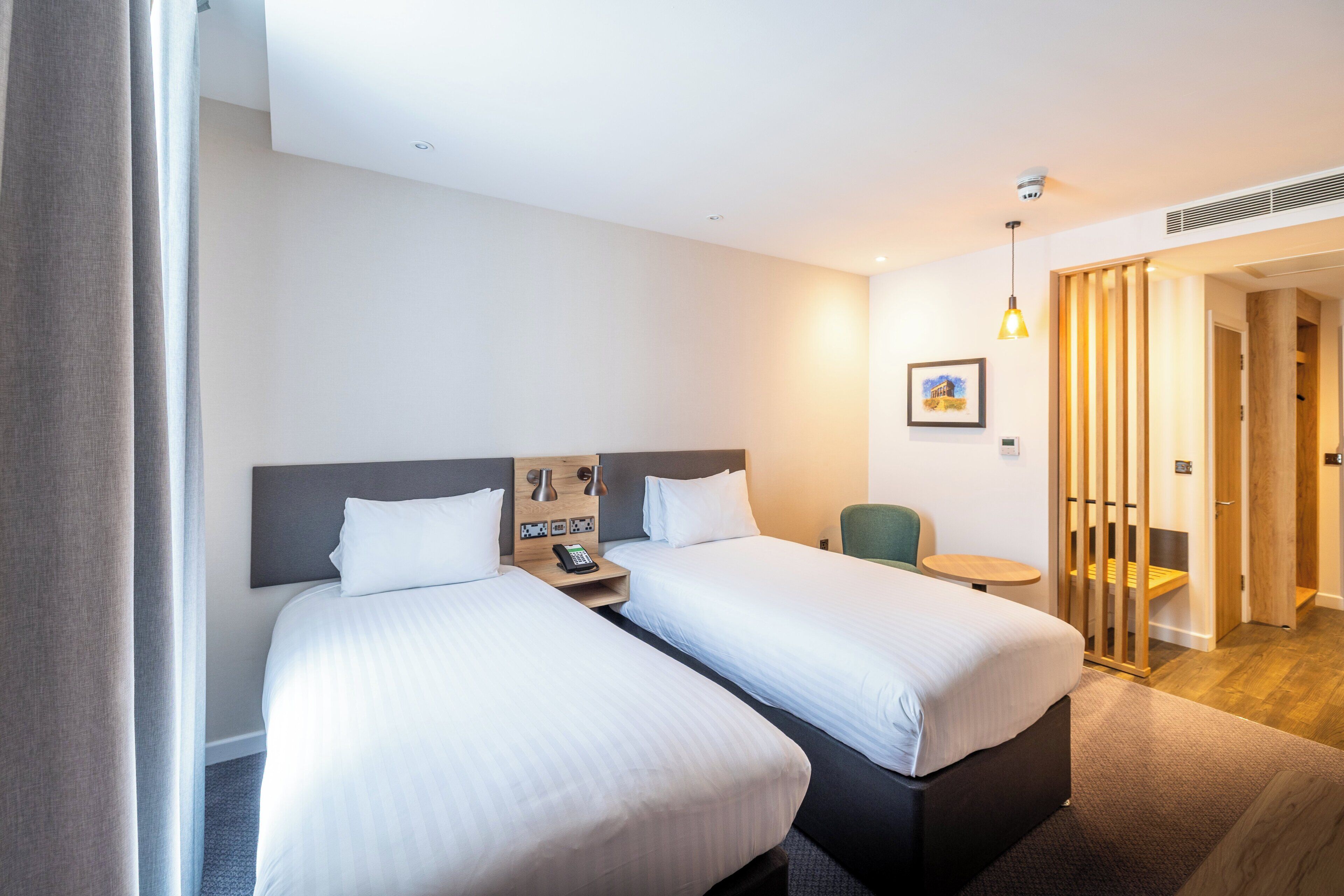 A hotel room with two beds, a small table, a chair, a desk, and a picture on the wall.